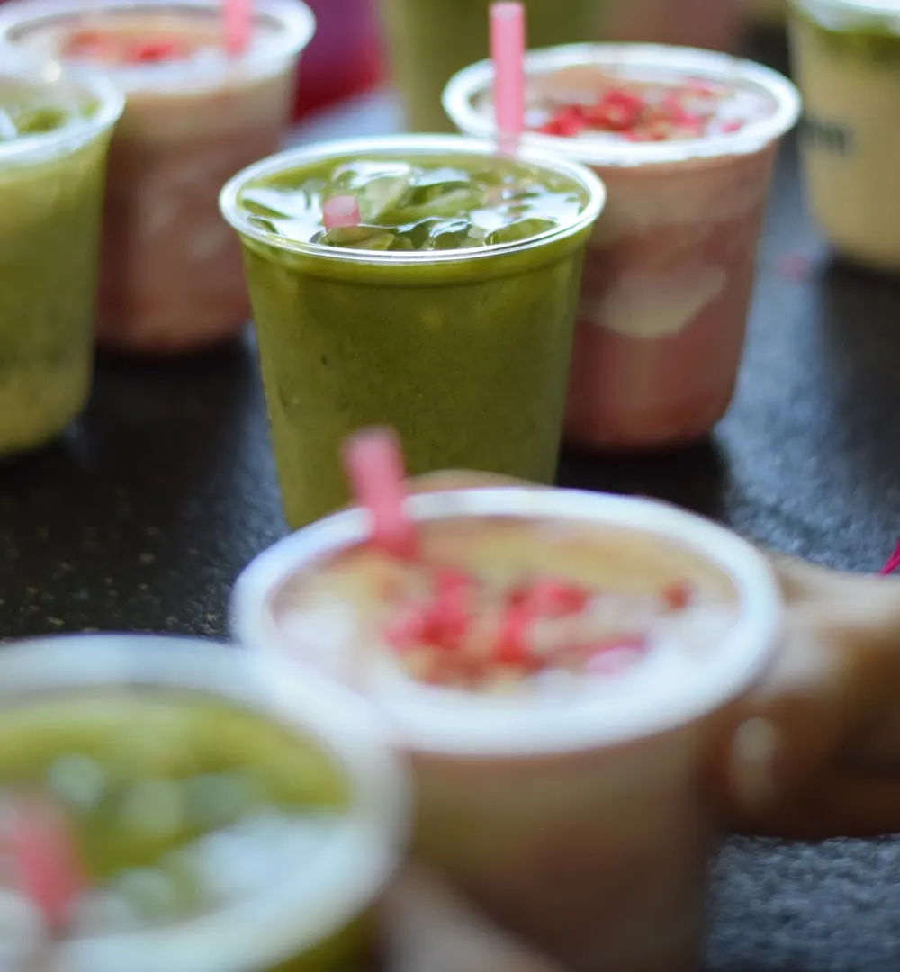 Vasos de matcha helado y de bebida de fresa con crema, con popotes rosas, sobre la barra negra de STAMINA